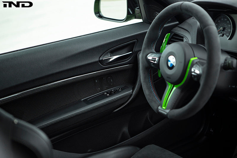 Interior view of Alpha N F87 M2 Carbon Door Card Set installed, showcasing sleek carbon fiber finish on vehicle door panels.