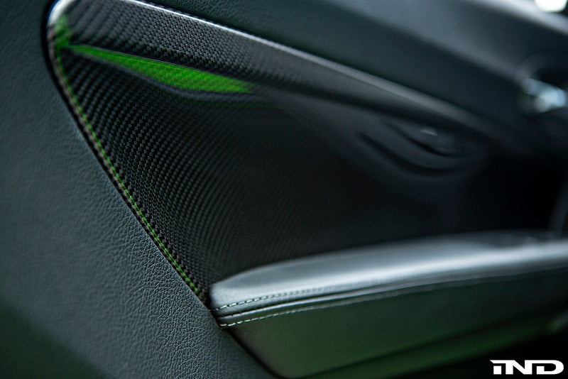Alpha N F87 M2 carbon interior door card set installed in a vehicle, showcasing sleek black carbon fiber finish.