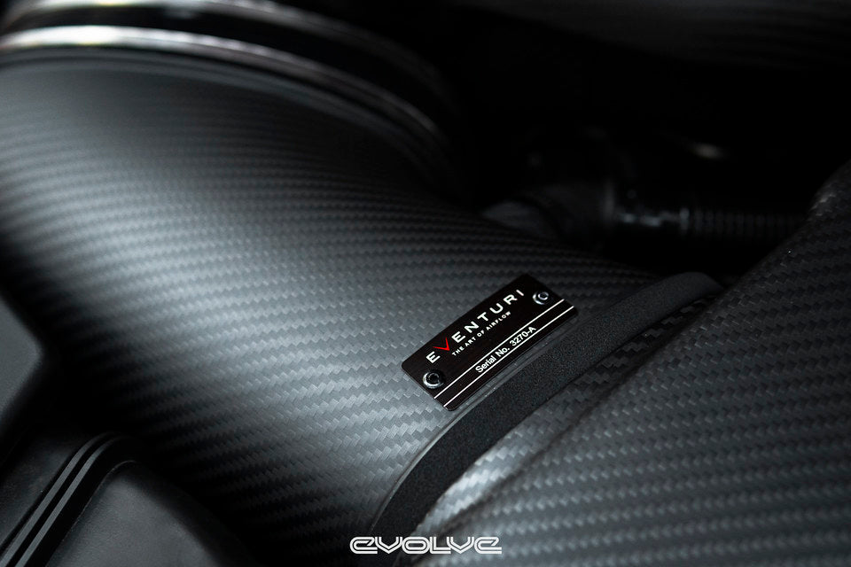 Close-up view of Eventuri matte carbon intake system duct connecting airbox and plenum installed in an E9X M3.