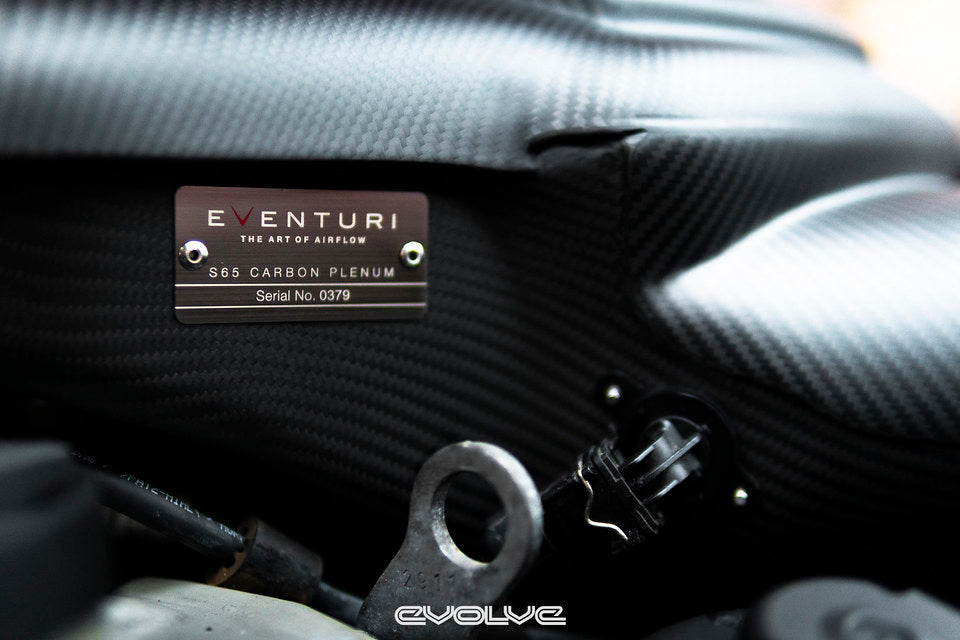 Close-up view of the Eventuri serial number plaque installed on the E9X M3 S65 Carbon Inlet Plenum in matte finish installed in an engine bay
