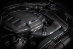 Eventuri black carbon inlet plenum installed in BMW E9X M3 (S65) engine bay, showcasing gloss finish and high-performance design.