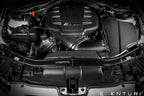 Eventuri black gloss carbon airbox lid installed on BMW E9X M3 S65 engine bay, showcasing performance car engine components.