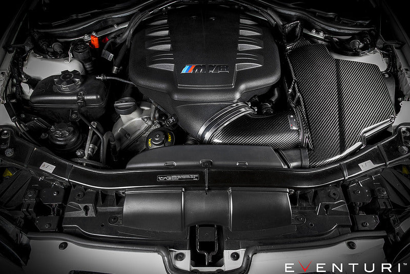 Eventuri black gloss carbon airbox lid installed on BMW E9X M3 S65 engine bay, showcasing performance car engine components.