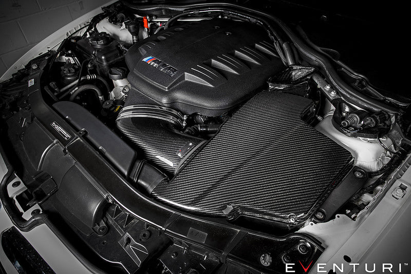 Eventuri black carbon airbox lid for BMW E9X M3 S65 engine bay, glossy performance air intake component.