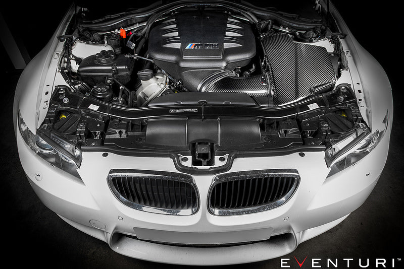 Eventuri black carbon airbox lid for BMW E9X M3 S65 engine bay, glossy performance upgrade for improved airflow and style.